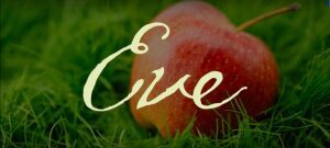 Close-up of a red apple with cursive text overlay on grass.